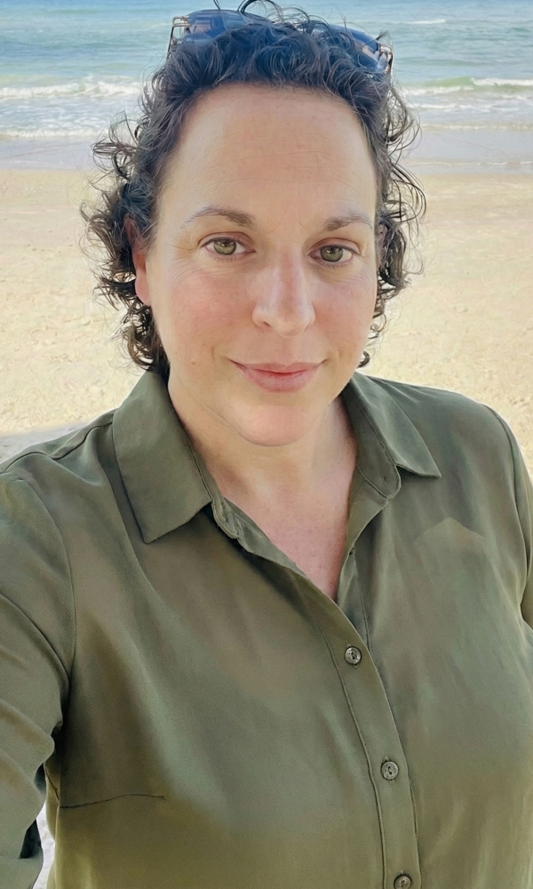 תמונת תדמית - ענבל בחולצת שיפון ירוקה עומדת בחוף הים